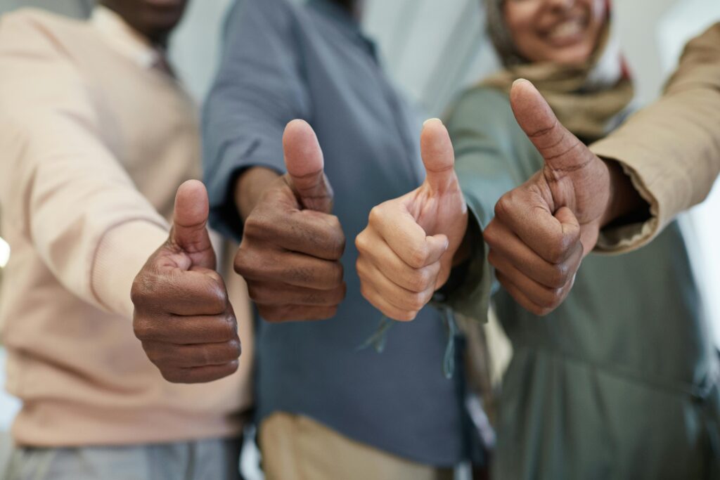 Close-up of a diverse team giving thumbs up indoors, symbolizing success and unity.